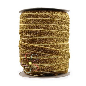May include: A spool of gold glitter velvet ribbon. The ribbon is wound tightly around the spool and has a subtle sheen.