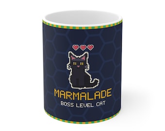 Puede incluir: Una taza de cerámica azul oscuro con un gato negro en pixel art con ojos amarillos y tres corazones rojos sobre la cabeza. El texto MARMALADE BOSS LEVEL CAT está impreso en fuente pixelada amarilla sobre un fondo de patrón hexagonal.