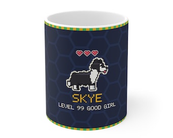 Puede incluir: Una taza de cerámica azul oscuro con un perro en pixel art, tres corazones rojos y el texto amarillo SKYE LEVEL 99 GOOD GIRL. La taza tiene un fondo de patrón hexagonal azul oscuro y un borde a cuadros verde y amarillo arriba y abajo.