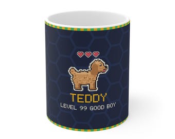 Puede incluir: Una taza de cerámica azul oscuro con un perro marrón en pixel art, tres corazones rojos y el texto amarillo "TEDDY" sobre el texto blanco "LEVEL 99 GOOD BOY". La taza tiene un patrón hexagonal azul oscuro y un borde verde y amarillo.