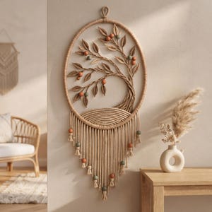 May include: An oval macrame wall hanging featuring a woven tree design with fabric leaves and small round beads in shades of terracotta and sage green. The piece includes a fringe base with hanging tassels and additional beads.