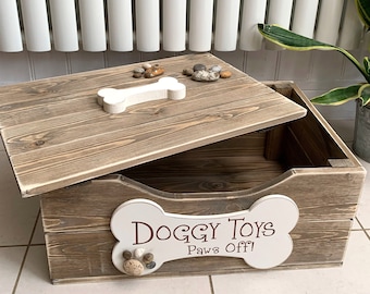 Peut inclure: Un coffre à jouets pour chien en bois avec un couvercle en forme d'os et une enseigne en forme d'os avec l'inscription "Doggy Toys Paws Off!". La boîte est en bois brun clair et a une finition vieillie. Le couvercle a une poignée en forme d'os blanche et de petites pierres.