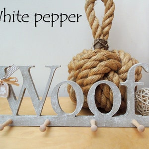 May include: A gray wooden "Woof" wall hook with three pegs, a paw print tag, and a decorative bow. The text "White pepper" is above the hook. A large rope knot and a woven ball are in the background.