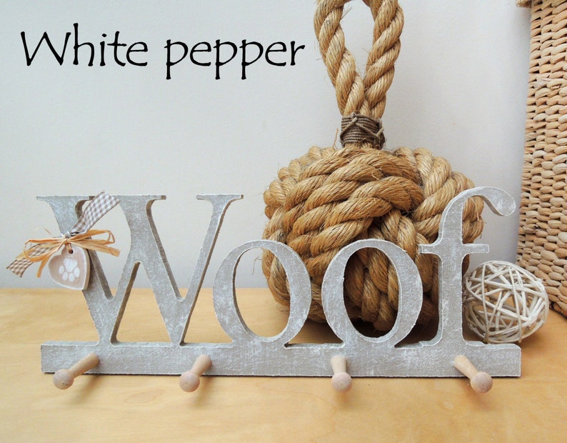 May include: A gray wooden "Woof" wall hook with three pegs, a paw print tag, and a decorative bow. The text "White pepper" is above the hook. A large rope knot and a woven ball are in the background.