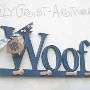 May include: A navy blue wooden wall-mounted coat rack spelling "Woof" with three pegs. A wooden heart-shaped tag with a paw print hangs from a blue and white paw print ribbon. The sign is for pet owners.