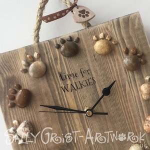 May include: A square wooden clock with a rope handle and paw print accents. The clock face features the phrase "time for WALKIES" and is decorated with stone paw prints. A wooden heart with a paw print hangs from the rope.