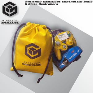 Puede incluir: Una bolsa de cordón amarilla con el logotipo y el texto de Nintendo GameCube en morado, acompañada de un mando de videojuegos amarillo de la marca Cirka en su embalaje de plástico transparente original para consolas GameCube y Wii.