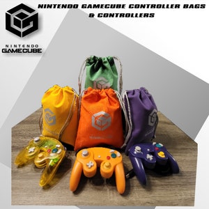May include: Four drawstring bags in green, yellow, orange, and purple, each featuring a silver Nintendo GameCube logo. Three video game controllers are placed in front: one translucent yellow, one solid orange, and one solid purple controller.