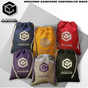 May include: Six fabric drawstring bags in blue, yellow, red, purple, beige, and black. Each bag features the white Nintendo GameCube logo and text printed on the front. The bags have light-colored cord closures and are arranged in a group.