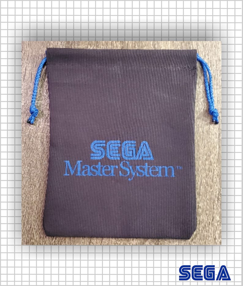 May include: A black fabric drawstring pouch featuring the blue embroidered text SEGA Master System centered on the front. The pouch includes two blue braided cords at the top for closure, providing a secure way to store small items or gaming accessories.