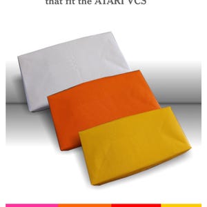 May include: Three rectangular dust covers for the ATARI VCS in white, orange, and yellow. The text Handcrafted Dust Covers that fit the ATARI VCS is displayed above the covers. A horizontal colour bar with pink, orange, red, and yellow is below.