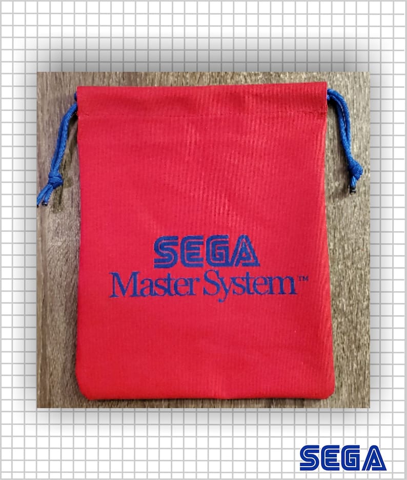 May include: A red fabric drawstring pouch featuring the blue embroidered text SEGA Master System centered on the front. The bag includes blue cord drawstrings on both sides, providing a secure closure for the rectangular storage accessory.