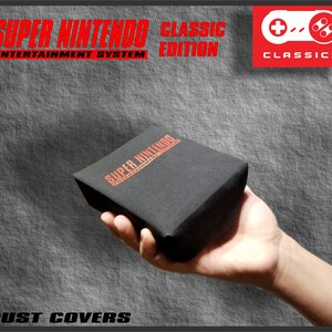 Op de afbeelding: Zwarte stofhoes voor een Super Nintendo Classic Edition console. De hoes heeft de tekst "SUPER NINTENDO ENTERTAINMENT SYSTEM CLASSIC EDITION" in het rood. Het woord "CLASSICS" staat in een rode doos rechtsboven.