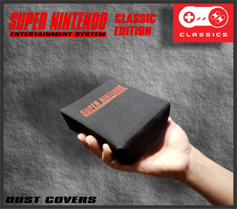 Op de afbeelding: Zwarte stofhoes voor een Super Nintendo Classic Edition console. De hoes heeft de tekst "SUPER NINTENDO ENTERTAINMENT SYSTEM CLASSIC EDITION" in het rood. Het woord "CLASSICS" staat in een rode doos rechtsboven.