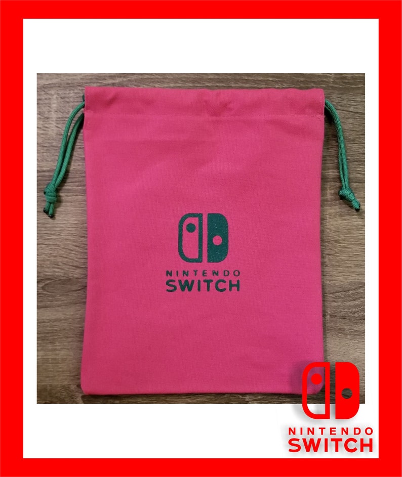 May include: A pink drawstring bag with a green drawstring. The bag features a green Nintendo Switch logo and the words "NINTENDO SWITCH" printed below. The bag is rectangular and made of a soft material.
