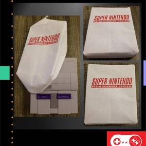 Op de afbeelding: Een Super Nintendo Entertainment System console met een witte beschermhoes met de rode tekst "SUPER NINTENDO ENTERTAINMENT SYSTEM". De afbeelding toont ook de aan/uit- en resetknoppen van de console.