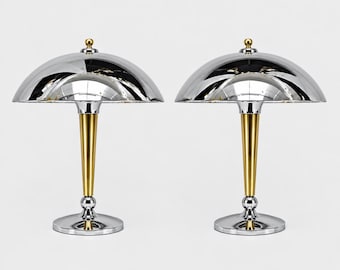 May include: A pair of table lamps featuring large, polished chrome dome shades, slender gold-toned tapered stems, and circular chrome bases. Each lamp is topped with a small gold-toned finial, creating a balanced, metallic aesthetic.