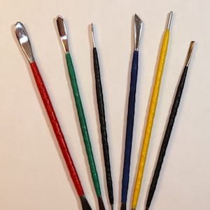 May include: Set of six sculpting tools with different shaped tips. The tools have black, blue, green, red, and yellow handles.