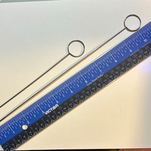 Könnte beinhalten: Zwei silberne Häkelnadeln mit runden Griffen. Die Nadeln liegen auf einem blauen und weißen Lineal mit dem aufgedruckten Text "Easy Read Ruler". Das Lineal ist in Zoll und Zentimetern gekennzeichnet.