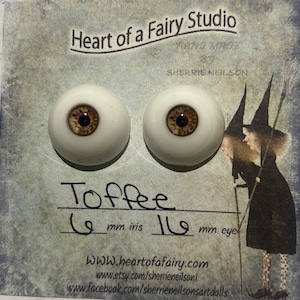 Puede incluir: Un par de ojos de muñeca de vidrio con iris marrón y esclerótica blanca. Los ojos tienen un diámetro de 16 mm y el iris de 6 mm. Los ojos están etiquetados como "Toffee" y son de Heart of a Fairy Studio.