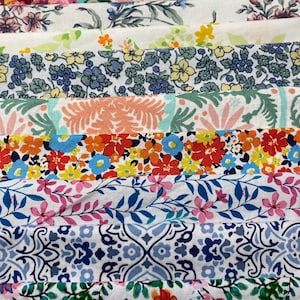 May include: A collection of fabric strips with various floral patterns in shades of pink, blue, green, and red. The fabric is arranged in a stack, with the top strip being a white background with pink and green floral designs.