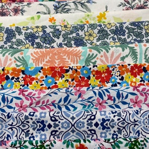 May include: A collection of fabric strips with various floral patterns in shades of pink, blue, green, and red. The fabric is arranged in a stack, with the top strip being a white background with a pink floral pattern.