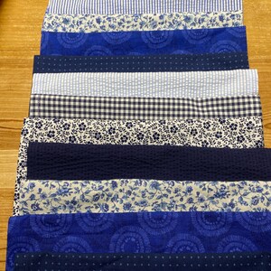 May include: A stack of 14 blue and white fabric squares with various patterns, including floral, gingham, and stripes. The fabric squares are arranged in a vertical stack, with the top square being a blue and white floral pattern.