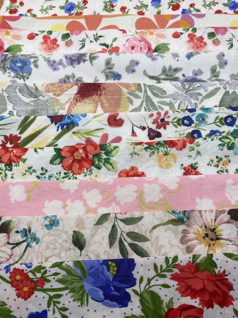 May include: A collection of 10 fabric strips with various floral patterns. The fabrics are in shades of pink, white, green, blue, and red. The patterns include small and large flowers, leaves, and dots.