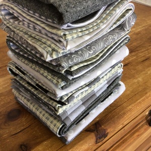 May include: A stack of gray and white patterned fabric napkins. The napkins are folded and stacked on a wooden surface.