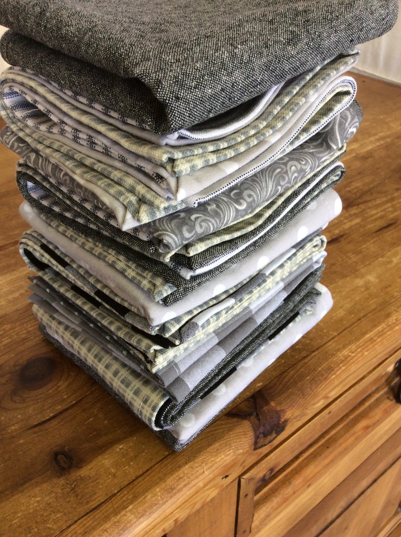 May include: A stack of gray and white patterned fabric napkins. The napkins are folded and stacked on a wooden surface.