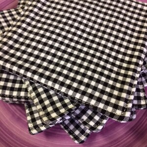 May include: A stack of black and white checkered fabric napkins. The napkins are folded and stacked on a purple plate.