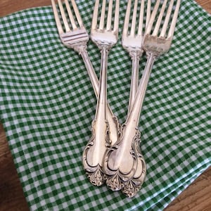 May include: Four silver forks with ornate handles are arranged on a green and white gingham tablecloth.