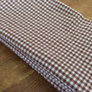 May include: A stack of brown and white gingham fabric napkins. The fabric has a checkered pattern.