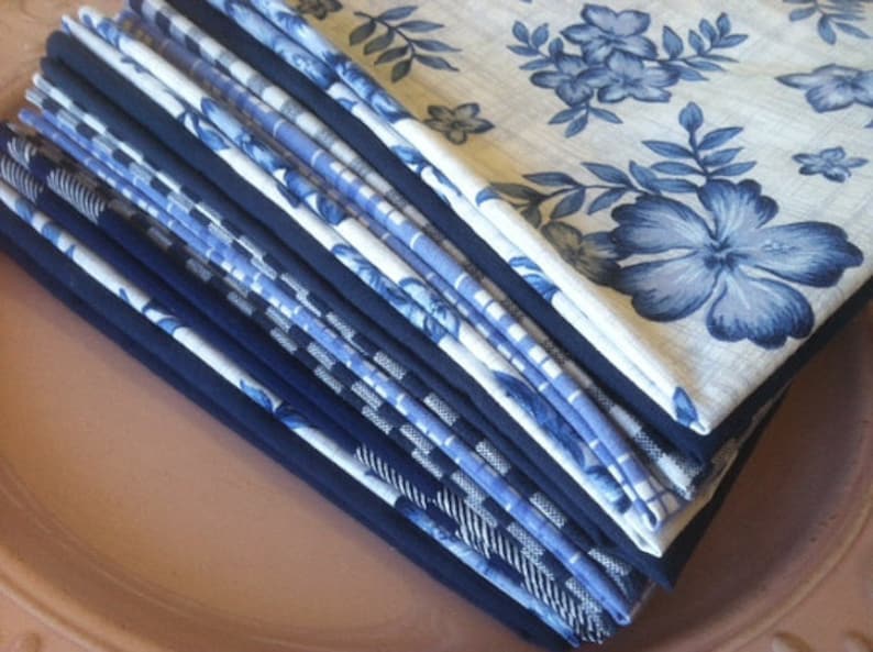 May include: A stack of blue and white patterned fabric napkins. The napkins have a floral design with blue flowers and leaves on a white background.