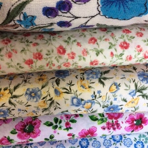 May include: Four different fabric swatches with floral patterns. The top swatch has a white background with purple and blue floral designs. The second swatch has a white background with small pink and green floral designs. The third swatch has a white background with yellow and blue floral designs. The bottom swatch has a white background with blue and green floral designs.