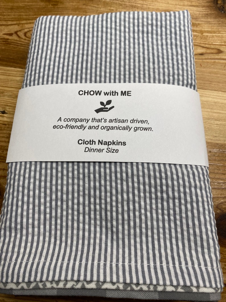 May include: Gray and white striped cloth napkins with the text "CHOW with ME" and "A company that's artisan driven, eco-friendly and organically grown. Cloth Napkins Dinner Size" on a white label.