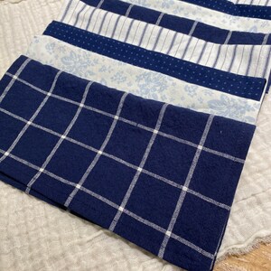 May include: A stack of seven blue and white patterned fabric napkins. The napkins are folded and arranged in a neat pile. The top napkin has a white grid pattern on a dark blue background.