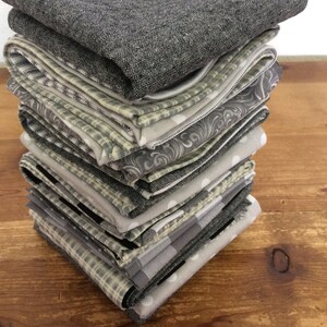 May include: A stack of 12 gray and white patterned fabric napkins. The napkins are folded and stacked on a wooden surface.
