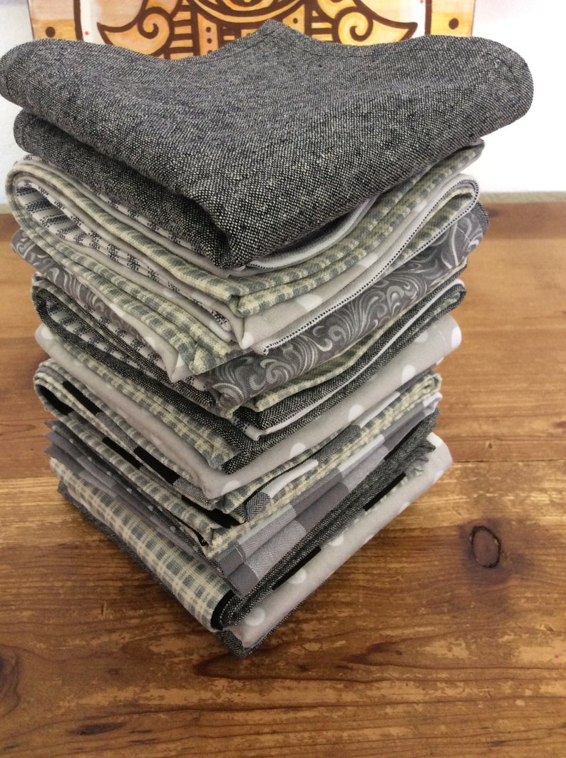 May include: A stack of 12 gray and white patterned fabric napkins. The napkins are folded and stacked on a wooden surface.