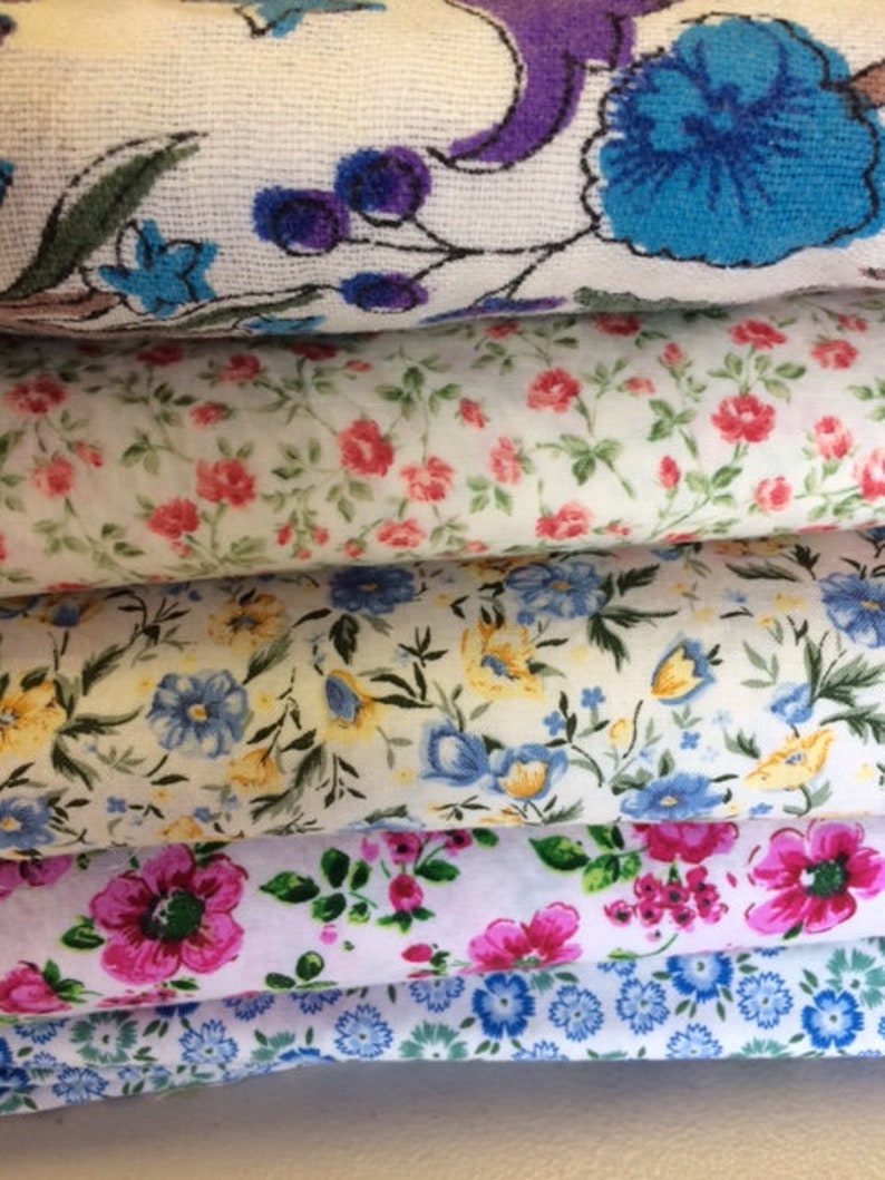 May include: Four different fabric swatches with floral patterns. The top swatch has a white background with purple and blue floral designs. The second swatch has a white background with small pink and green floral designs. The third swatch has a white background with yellow and blue floral designs. The bottom swatch has a white background with blue and green floral designs.