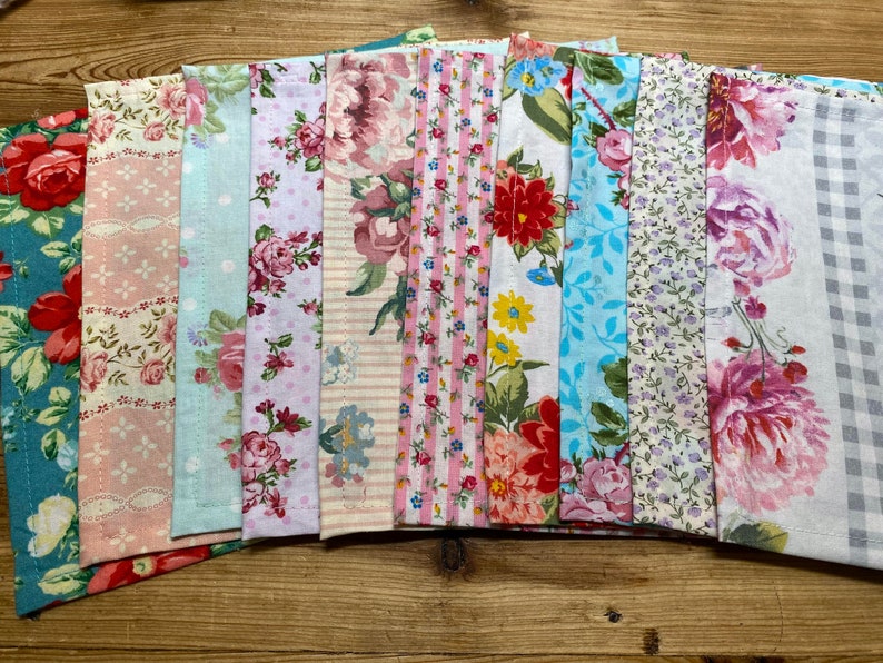 May include: A collection of 10 fabric swatches with floral patterns in shades of pink, blue, and white. The fabrics have a variety of textures, including gingham, stripes, and polka dots.