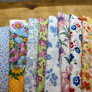 May include: Assortment of 10 fabric swatches featuring floral patterns in various colors, including blue, pink, yellow, and green. The fabrics are arranged in a row, with the edges folded over.