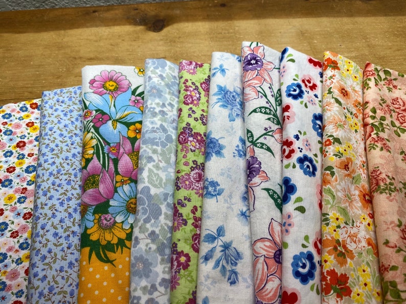 May include: Assortment of 10 fabric swatches featuring floral patterns in various colors, including blue, pink, yellow, and green. The fabrics are arranged in a row, with the edges folded over.