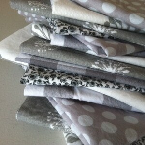May include: A stack of gray and white kitchen towels with various patterns, including polka dots, floral designs, and geometric patterns.