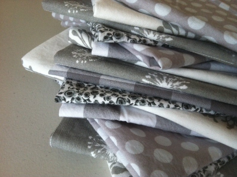 May include: A stack of gray and white kitchen towels with various patterns, including polka dots, floral designs, and geometric patterns.