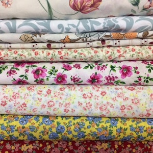May include: A stack of eight fabric rolls with various floral patterns. The fabrics are in shades of pink, yellow, red, and blue.