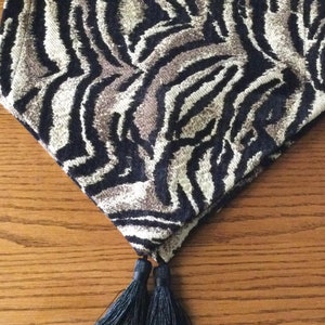May include: A black and beige zebra print table runner with black tassels.