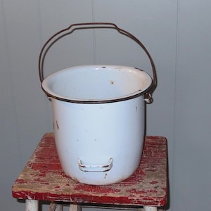 May include: White enamel bucket with a rusty metal handle. The bucket is sitting on a red wooden stool.