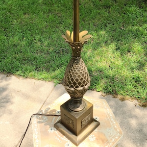 May include: A gold pineapple-shaped table lamp with a white ruffled lampshade. The lamp is on a patterned tile surface.