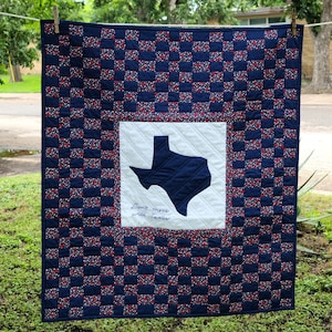 May include: A handmade quilt with a navy blue background and a repeating pattern of red and white floral squares. The center features a white square with a navy blue Texas outline and the text "Don't mess with Texas."